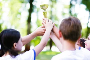 Crianças comemorando ao ar livre enquanto seguram juntas um troféu dourado, simbolizando a vitória em um concurso cultural