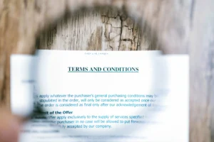 Documento impresso com o título 'TERMS AND CONDITIONS' em destaque, parcialmente ampliado por uma lupa, sobre uma superfície de madeira rústica.