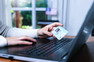 Pessoa usando notebook e segurando um documento de identificação, simbolizando verificação de CPF inválido e checagem de dados para participação em sorteios online e promoções seguras.