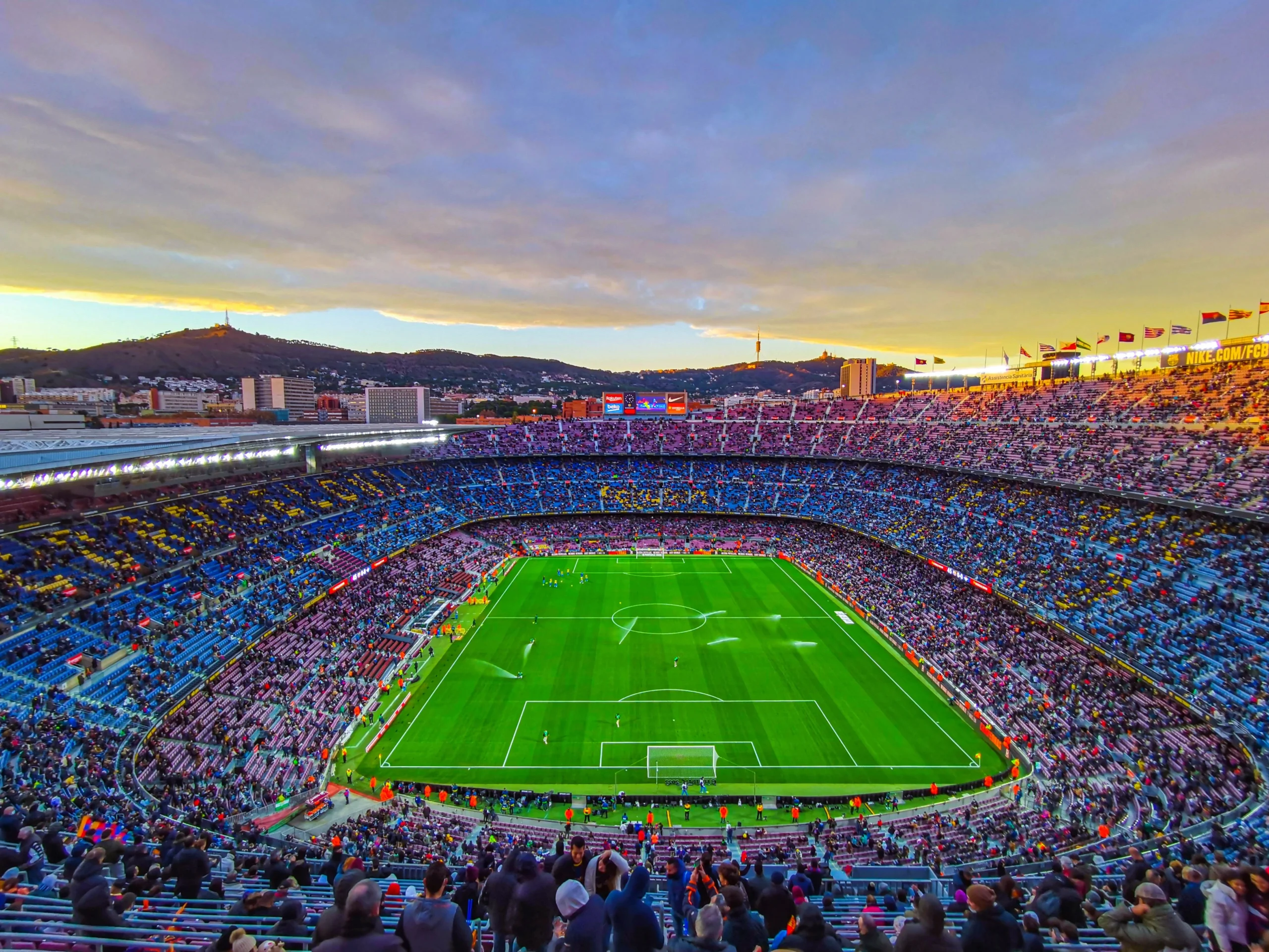 Vista panorâmica de um grande estádio de futebol lotado ao pôr do sol, com o campo verde preparado para a partida, atmosfera vibrante que representa a expectativa de sorteio da Copa do Mundo e grandes jogos internacionais.