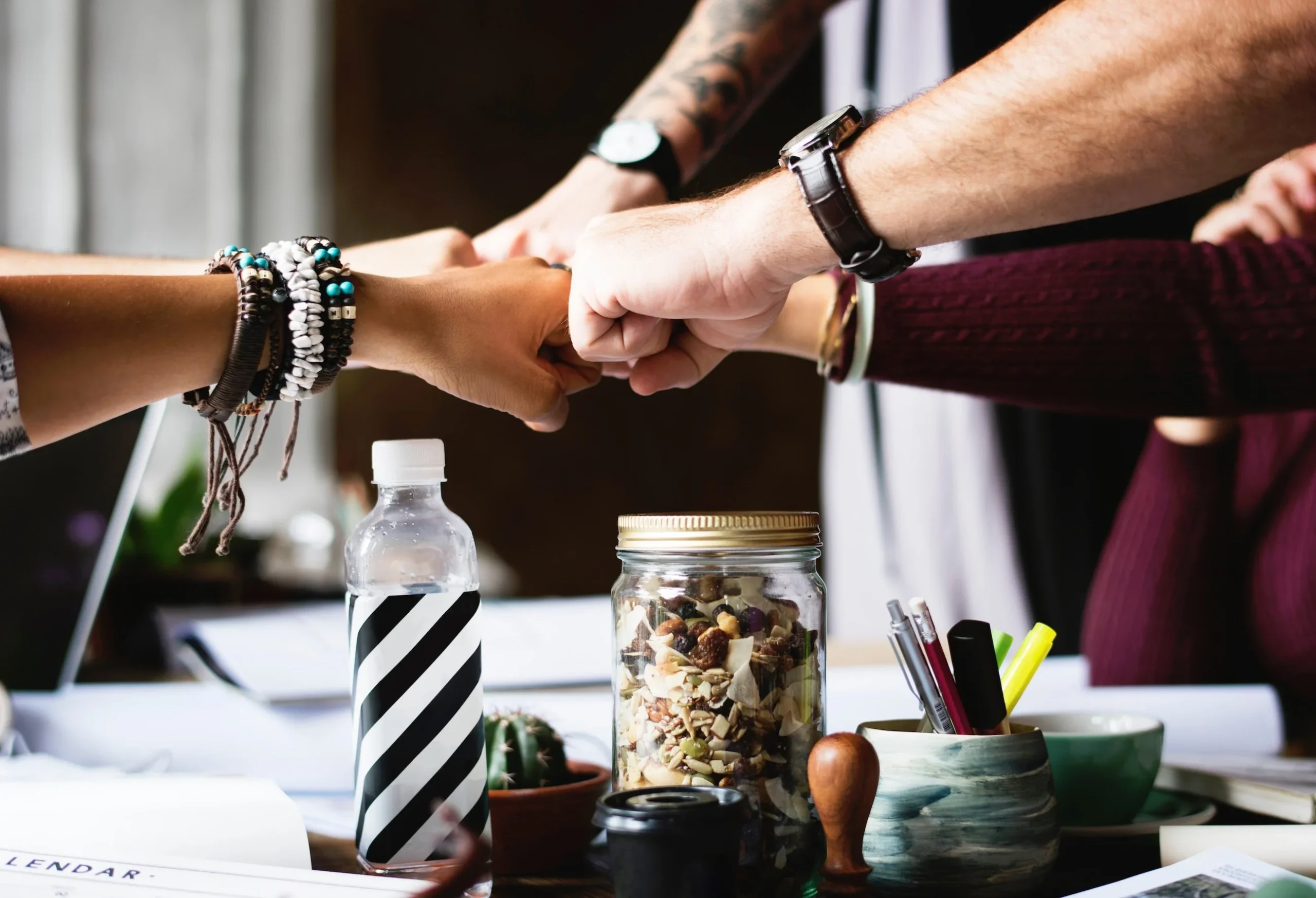 Grupo de pessoas fazendo gesto de união com punhos juntos sobre mesa com snacks e materiais de escritório, conceito de trabalho em equipe para campanhas de rifas
