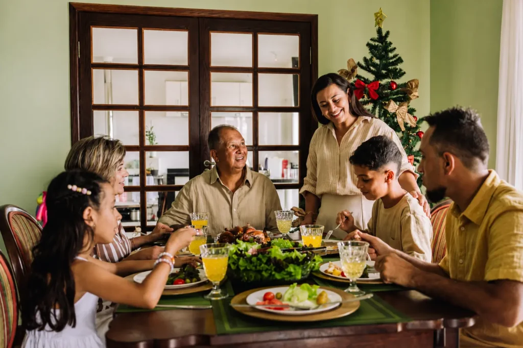 Família reunida à mesa para a ceia de Natal, com pratos de comida, bebidas e árvore de Natal decorada ao fundo