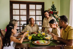 Família reunida à mesa para a ceia de Natal, com pratos de comida, bebidas e árvore de Natal decorada ao fundo